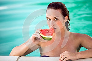 Seductive woman in pool refreshes with piece of watermelon