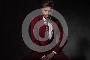 Seductive young man wearing grena suit sitting