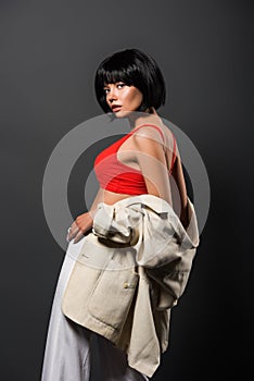 seductive young woman with bobbed hair in red crop top and jacket looking at camera