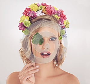 See beauty in a new light. A young woman with flowers in her hair covering her one eyes with a leaf.