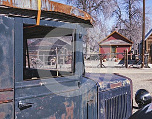 See jalopy old car truck. Through window see old house buildings.