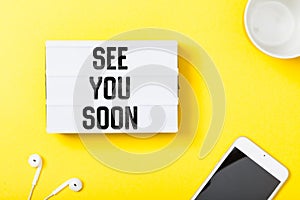 See you soon word in light box on office table flat lay photo