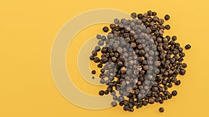 Seeds of black pepper pile on top on a yellow background, close-up, copy space