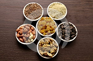 Seeds, nuts and dried fruits are poured into round salad bowls that stand in a circle against a dark background