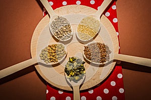 Seeds on wooden spoons which are lying at the round cutting board and red napkin - sesame, linseed, pumpkin and sunflower seeds, g