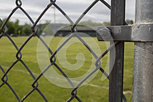 Seeing a baseball green grass diamond field through the classic diamond-shaped fence