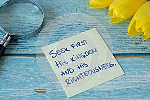 Seek first His kingdom and righteousness, handwritten biblical verse on a note with magnifying glass and yellow tulips on wood photo