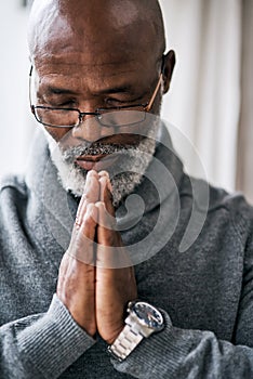 Seeking guidance from above. a handsome senior man praying while sitting in his home.