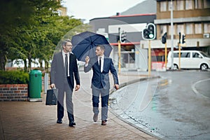 Seeking new opportunities in the city. Shot of two corporate businessmen travelling through the city on a rainy day.