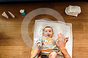 Seen above the face of a smiling baby while his dad`s hands change his dirty diaper