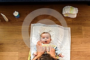 Seen above the face of a smiling baby while his dad`s hands change his dirty diaper