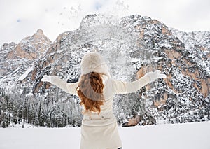 Seen from behind woman in coat and hat throwing snow outdoors
