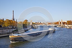 Seine river view with barge, Eiffel tower and Alexander III bridge in a sunny autumn day in Paris