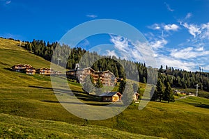 Seiser Alm, Italy - Tyrolean wooden hotels and chalets and green fields at Alpe di Siusi on a sunny summer day with blue sky