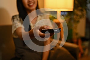 Select focus on woman hand holding remote control, watching TV at night. Entertainment and hobby concept