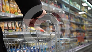 SELECT PRODUCTS IN THE SUPERMARKET. SLOW MOTION. A look next to a moving empty cart in a store. Man`s hand. Close-up