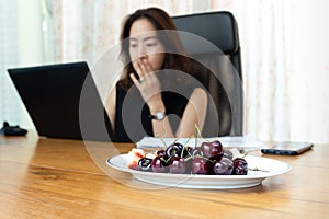 Selected focus on cherry fruit in a plate with business woman working on laptop computer.