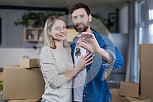 Selected focus, married couple man and woman happy together, hugging, holding the keys to their new apartment, housewarming, close