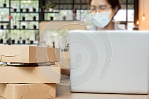 Selected focus parcel box on table with woman wearing medical mask work on laptop at home.