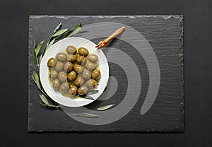 Selected olives in a white plate decorated with natural olive tree branches on a dark background.