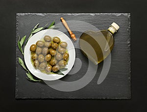 Selected olives in a white plate decorated with natural olive tree branches and olive oil heart bottle.