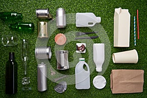 A selection of garbage for recycling. Segregated glass, metal, plastic and paper on green grass background.