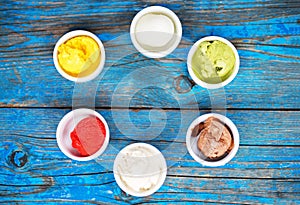 Selection of gourmet flavours of Italian ice cream in vibrant colors served in individual porcelain cups on an old rustic wooden t