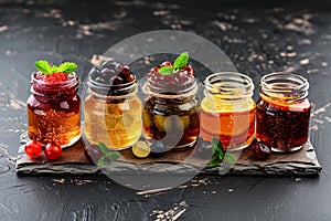 Selection of homemade jams and natural honey gleams on dark surface