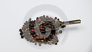 A selection of peppercorns with a measuring spoon on a white background