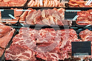 Selection of quality meat at a butcher shop, butchered pork in a refrigerated display case under glass