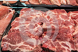 Selection of quality meat at a butcher shop, butchered pork in a refrigerated display case under glass, close up