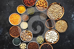 Selection of superfoods, legumes, cereals, nuts, seeds in bowls on black background. Superfood as chia, spirulina, beans, goji