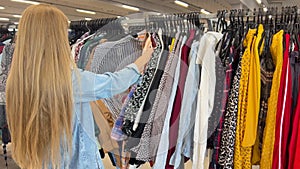 Selection of used clothes in a second-hand store. A woman buys inexpensive clothes