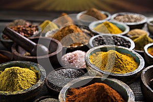 A selection of various colorful spices on a wooden table in bowl