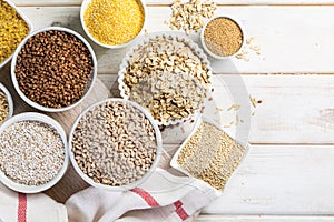 Selection of whole grains in white bowls - rice, oats, buckwheat, bulgur, porridge, barley, quinoa, amaranth,