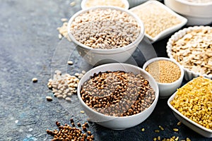 Selection of whole grains in white bowls - rice, oats, buckwheat, bulgur, porridge, barley, quinoa, amaranth