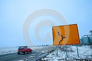 Selective blur on a fast car with a speed blur in winter, with a snowy rural environment, in a european road, with a blank yellow
