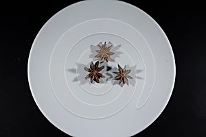 Selective blur on star anise, three stars, isolated on a white grey plate on a black background. Anise, or aniseed, is a spice,