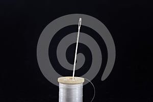 Studio shot of a white thread reel and a sewing needle isolated on a black background. Spool (or reel), thread