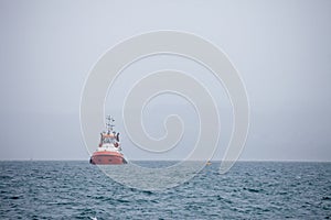 Selective blur on a tugboat, alone, manoeuvering in a grey sea, during a bad weather condition, with smog and fog.