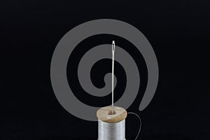 white thread reel and a sewing needle isolated on a black background in a studio shot. Spool (or reel), thread