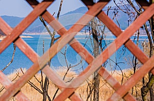 Selective blurring lattice work fence with lake and trees in focus in background.