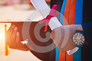 Selective and close-up focus of a university graduate holds a degree certificate and graduation cap celebrates in the graduation c