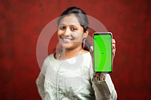 Selective focous on smartphone, Happy smiling Indian girl in traditional dress showing mobile phone with mock up green screen for