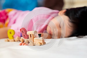 Selective focus. Adorable child fell asleep with a wooden figure train toy Number in her hand while the little girl sleepy.