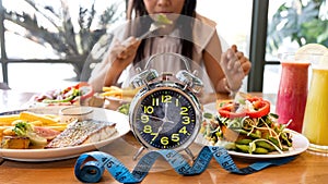 Selective focus of Alarm clock with woman eating a healthy food as Intermittent fasting, time-restricted eating