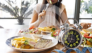 Selective focus of  Alarm clock with woman eating a healthy food as Intermittent fasting, time-restricted eating-Diet breakfast