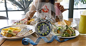 Selective focus of  Alarm clock with woman eating a healthy food as Intermittent fasting, time-restricted eating-Diet breakfast