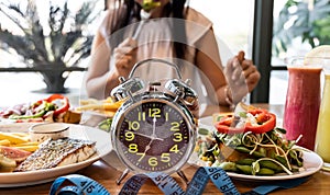 Selective focus of Alarm clock with woman eating a healthy food as Intermittent fasting, time-restricted eating-Diet concept