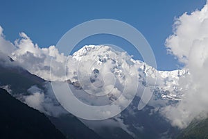 Selective focus Annapurna South peak with white first snow and fog with noise and grain in bright sunlight